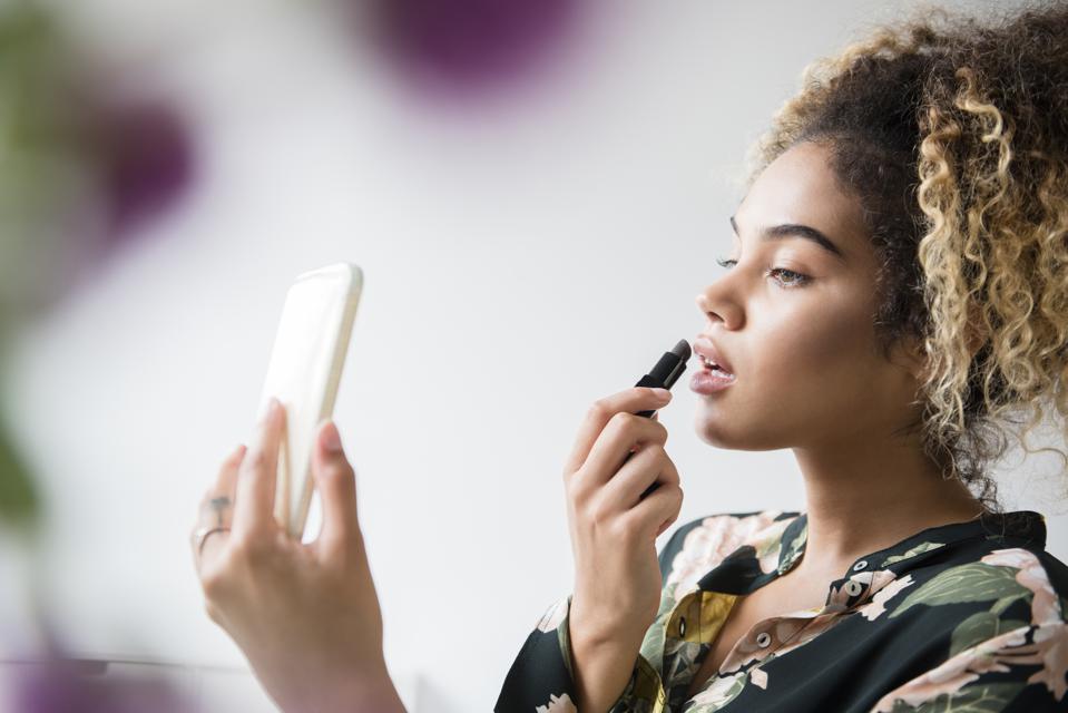 lady applying lipstick using her phone as a mirror